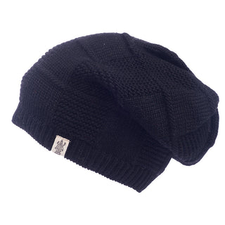 The Checkered Slouch, a black knit beanie featuring a textured pattern and a small rectangular logo label stitched at the edge, is displayed against a white background, evoking the artisanal quality of handmade wool hats from Nepal.