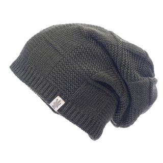 A side view of the Checkered Slouch, a dark green knitted beanie hat with a textured pattern. This wool hat, handmade in Nepal, offers a slouchy style and features a small white tag with a logo near the brim.