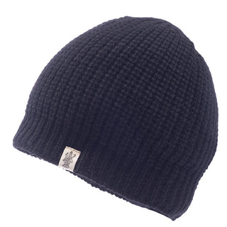 The Cardigan Knit Beanie, a black handmade hat from Nepal crafted from 100% wool, features a light-colored tag with a small emblem and is displayed against a white background. The beanie boasts a textured, ribbed pattern.