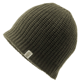 A close-up of the Cardigan Knit Beanie, a dark green, ribbed knit hat handmade in Nepal. Crafted from 100% wool, the beanie features a small fabric tag with a logo or design near its edge. The hat is positioned against a white background.