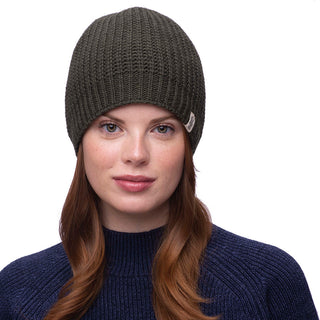 A person with long brown hair is wearing a dark green Cardigan Knit Beanie made of 100% wool and a navy blue sweater. The background is plain white.