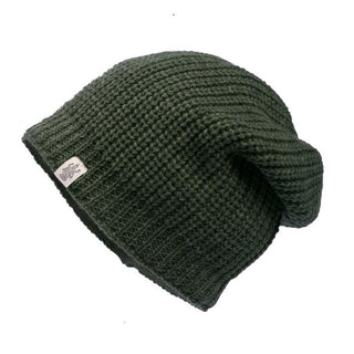 The "Cardigan knit slouch" is a dark green, handmade Nepali beanie featuring a slouchy fit and ribbed texture. Crafted from 100% wool, it has a cozy cardigan-knit style with a small rectangular white label on the side containing indistinct text or logo.