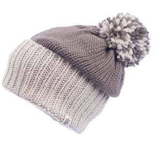 The Masha Pom Slouch is a handmade, knitted beanie hat featuring a brown top section adorned with a pom-pom, and a lighter beige ribbed lower section. Crafted from soft wool, it also includes a small logo tag attached to the ribbed area.