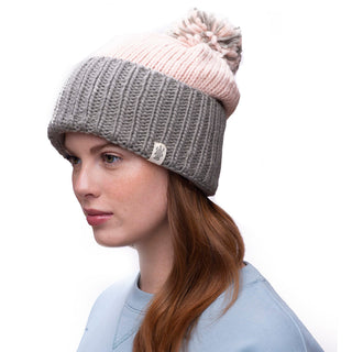 A person with long hair is shown in profile wearing the handmade Masha Pom Slouch beanie, featuring a color block design with light pink at the top and gray at the bottom, topped with a pom-pom. They are also wearing a light blue sweatshirt.