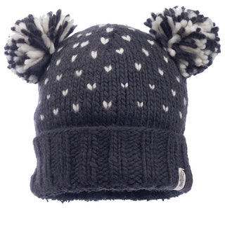 The Double Pom Kira Hat, crafted in Nepal from soft wool, is a knitted navy blue accessory embellished with white heart patterns and finished with two fluffy pom-poms. It includes a folded brim and a small fabric tag on the side.