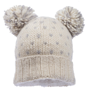 The Double Pom Kira Hat, handmade in Nepal, is a cream-colored knitted masterpiece crafted from wool. It features two large pom-poms on top and subtle gray speckles, with a ribbed band at the bottom for added warmth and comfort.