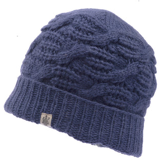 The Side Cable Knit Beanie is a blue hat featuring a ribbed cuff and a textured cable knit pattern on the main body. Handmade in Nepal from 100% wool, it includes a small tag with an emblem sewn onto the cuff.