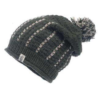 Ferry Slouch Hat is a knitted beanie in green with cream-colored vertical stripes and a pom-pom on top, crafted from soft merino wool. This handmade piece from Nepal features a small fabric tag near the brim. Its warm and cozy texture makes it perfect for cold weather.
