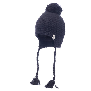 The Verona Earflap Hat is a black knitted winter accessory featuring wool earflaps, braided tassels, and a pom-pom on top. It includes a cozy sherpa lining and has a small tag sewn on the side for that authentic handmade Nepal touch.