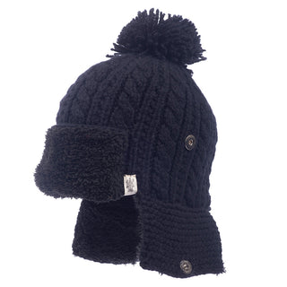 The Sherpa Trapper Hat w/ Pom is a black knitted hat, complete with a pom-pom on top and a cozy, furry lining. Handmade in Nepal, this stylish hat includes ear flaps with buttons on the sides for added warmth and flair.