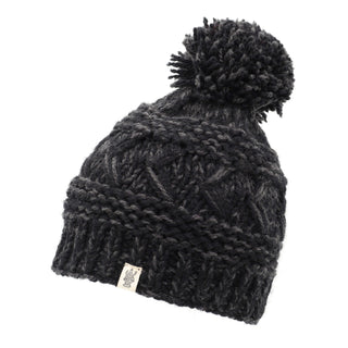 The Reverse Cross Pom Pom Hat is a dark gray, knitted beanie adorned with a pom-pom on top. It showcases various intricate knitting patterns and textures, and includes a small tag featuring a design or logo on the front.