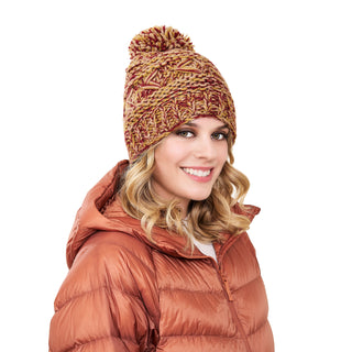 A woman smiling and wearing a warm, Reverse Cross Pom Pom Hat with a mix of red and beige colors and an orange puffer jacket. She has blonde, wavy hair, is facing the camera, and is standing against a plain white background.