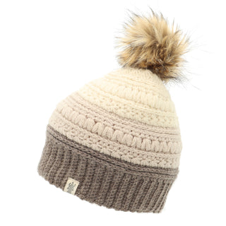 The Stripe Flower Fur Pom Pom is a knitted winter accessory in a cream and beige color palette, featuring a brown band at the bottom. It showcases faux fur on top, a textured pattern, and a small fabric tag with a logo on the brown band.