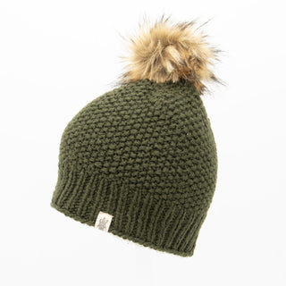 The Moss Fur Pom Pom Hat is a knitted green beanie featuring a ribbed edge and adorned with a brown and tan faux fur pom-pom on top. It has a small tag showcasing the logo sewn near the bottom edge, set against a white background.