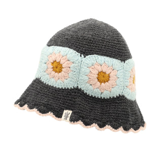 Introducing the Mushroom Hat: a stylish, hand-knit headpiece made from merino wool. It features a dark gray crown and brim, accented by a light blue band adorned with large cream and yellow flower motifs. The brim's edge is trimmed with a delicate scalloped light pink border for added charm. It also includes a small white tag with a simple design attached to the band.