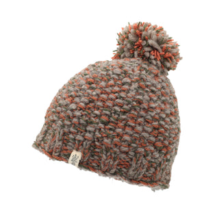 The Chunky Pom is a knitted wool hat featuring a mixed color pattern of grey, orange, and green. It has a pom-pom on top and includes a small tag with a logo near the brim. The hat boasts a chunky texture with visible stitching.