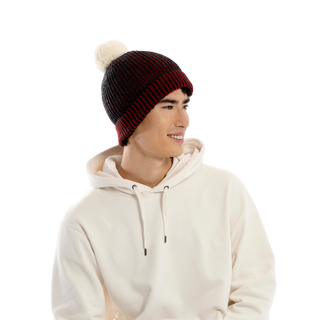 A person wearing a white hoodie and an Allen Pom Hat featuring a red and black knit design smiles while looking to their left, set against a plain black background.