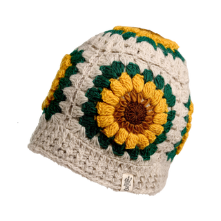 The Sunflower Hat is a handmade crocheted hat with a large yellow, green, and brown sunflower motif on a beige background, finished with a small fabric tag on the brim.