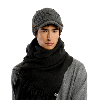 A person wearing a Broadway Hat in gray, featuring buttons on the sides, paired with a gray scarf wrapped around their neck and a gray jacket. The background is solid black.