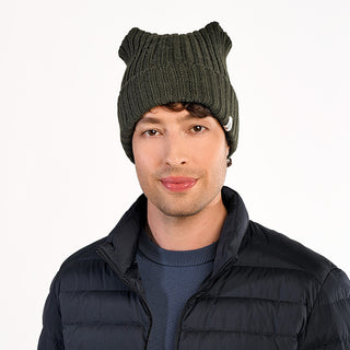 A man wearing the Ely Hat in dark green wool, a blue crew neck sweater, and a black puffer jacket with faux sherling lining stands against a plain white background.