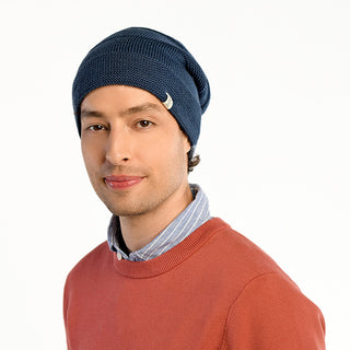 Wearing the Edgar Slouch beanie, a person in a blue and white striped shirt and rust sweater looks at the camera against a white background. The cozy and stylish wool hat is perfect for cooler days.
