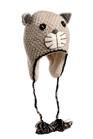The Crochet Shmil the Cat Hat is a hand-knitted design made from 100% wool in Nepal. It showcases small ears, black button-like eyes, and a white snout with whiskers. The hat includes ear flaps with braided tassels ending in pom-poms and is predominantly beige with black accents.