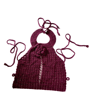 Introducing the "Collar Top": A maroon crocheted halter top featuring a circular neckline, enhanced with a decorative flower design at the center. It includes long ties for securing around the neck and back, along with an open stripe detail down the middle front for an elegant touch.