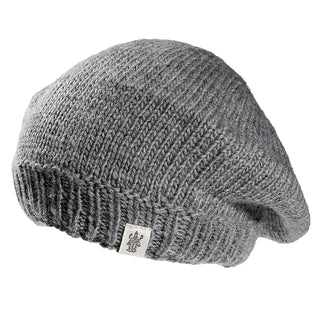 The Abbey Hat is a gray knitted wool beret with a ribbed edge and a small rectangular fabric tag featuring an emblem, shown against a white background.