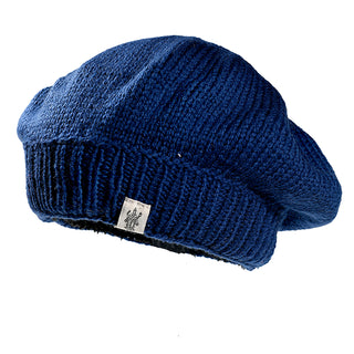 The Abbey Hat is a blue knit beret with a ribbed band and a small white logo tag, displayed against a white background.