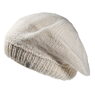The Abbey Hat is a cream-colored knitted beret featuring a ribbed band and a small rectangular fabric tag on the edge.