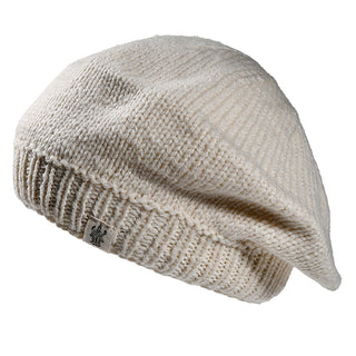 The Abbey Hat is a cream-colored knitted beret featuring a ribbed band and a small fabric tag on the edge, shown against a white background.