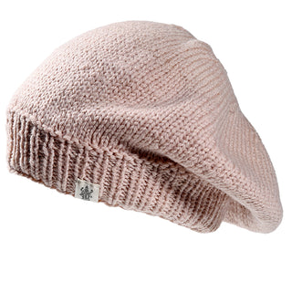 The Abbey Hat is a light pink knitted beret with a ribbed band and a small logo fabric tag sewn onto the edge.