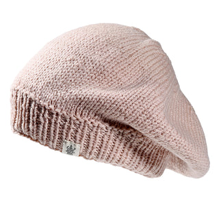 The Abbey Hat is a light pink knitted beret with a ribbed edge and a small rectangular fabric tag featuring a decorative emblem, shown on a white background.