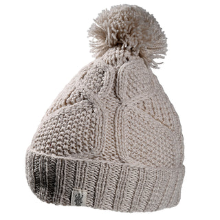 The Cedar Hat is a beige cable-knit winter beanie with a folded brim, pom-pom on top, and a small logo fabric tag on the brim.