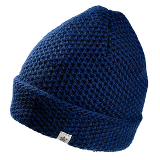 The Baltic Hat is a dark blue knitted beanie featuring a textured pattern and folded brim, accented by a small white logo tag on the brim. It is showcased against a plain white background.