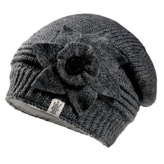 The Monroe Hat is a gray knitted beanie with a ribbed edge, featuring a large felt flower applique and a small fabric logo tag, displayed against a white background.