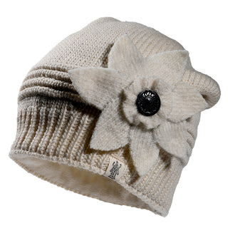The Monroe Hat is a cream-colored knit beanie with ribbed detailing, a large layered felt flower featuring a black button at the center on the side, and a small fabric tag on the brim.