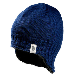 The Dakota Hat is a blue knit winter hat with a ribbed edge and black fleece lining, featuring a small white tag with a crest design on the front. It is shown against a plain white background.