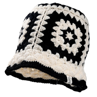 The Milie Hat is a black and white crochet bucket hat featuring a geometric granny-square pattern and a small white fabric tag sewn onto the brim.