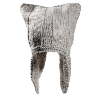 The Ezra Hat is a gray knitted winter hat featuring two pointed corners on top and long ear flaps on each side. It has a varied knit pattern, and its thick fabric offers warmth and comfort.