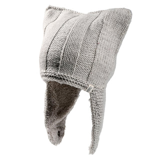 The Ezra Hat is a light gray knit winter hat with two pointed corners on top, long ear flaps on each side, and features ribbed and textured knitting patterns.