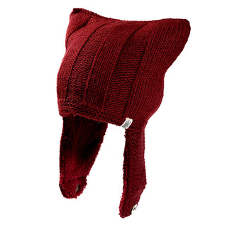 The Ezra Hat is a red knitted hat with two pointed corners resembling cat ears and long earflaps on each side.