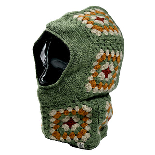 A mannequin displays the Ryan Hood, a green crochet balaclava featuring granny squares in green, cream, rust, and beige. It covers the head and neck while leaving the face open.