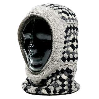A mannequin head displays the Ryan Hood, a crocheted hood featuring a geometric pattern in gray, black, and white. It fits snugly around the head and neck with an open face and textured stitches.