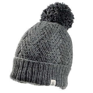 The Aspen Hat is a gray knitted beanie with a ribbed brim, a large pom-pom on top, and a small fabric tag on the lower edge.
