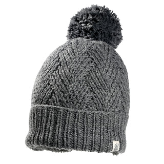 The Aspen Hat is a gray knitted beanie with a thick ribbed brim, pom-pom on top, chevron knit pattern, and a small white tag on the bottom edge.