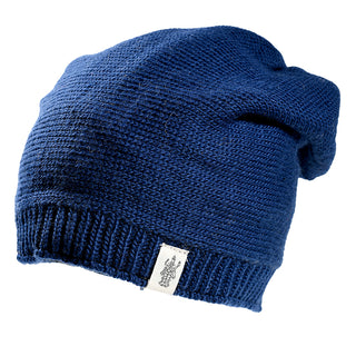 The Dekalb Slouch is a unisex blue Merino wool knitted beanie with a ribbed edge and a small white tag with embroidered detail, shown against a white background—a cozy cold-weather hat.