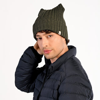 A person wearing the Ely Hat, a dark green wool beanie handmade in Nepal, and a black puffer jacket poses against a plain white background with one hand touching the back of their head.