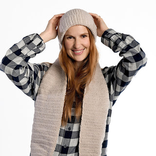 A person smiles, touching their Oversized Ear Beanie, paired with a matching scarf and a black-and-white plaid shirt, against a plain white background.