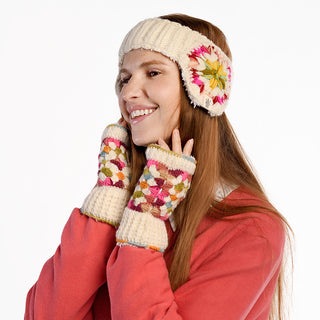 A woman with long brown hair models the Avon Headband—a handmade wool accessory from Nepal with colorful floral patterns—plus matching fingerless gloves. Smiling in a coral pink top, she poses against a plain white background.